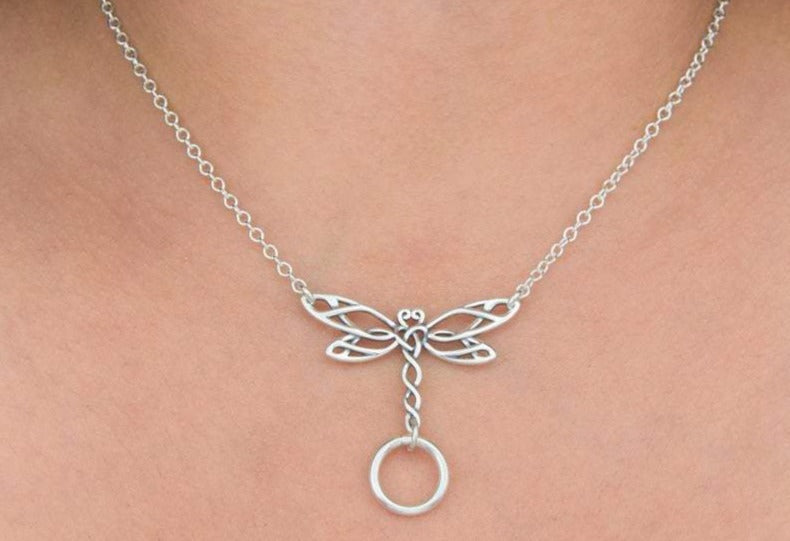 A sterling silver day collar necklace with a Celtic dragonfly design and a solid ring at the center, worn on a person.